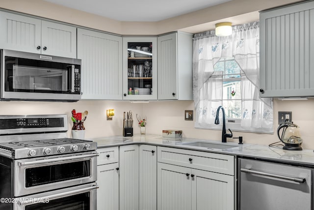 kitchen featuring stainless steel appliances, gray cabinets, sink, and light stone countertops