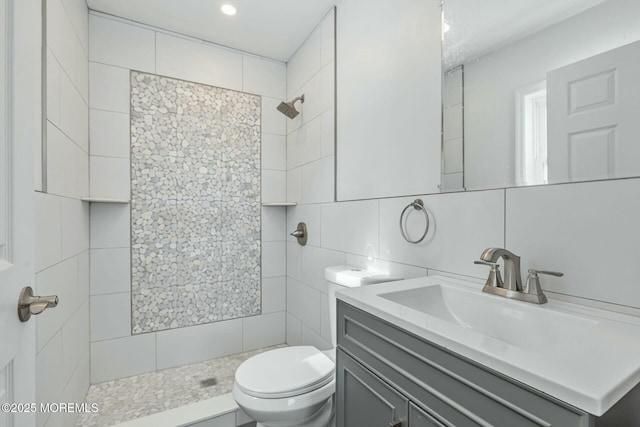 bathroom featuring a tile shower, tile walls, decorative backsplash, vanity, and toilet