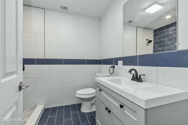 bathroom featuring tiled shower, vanity, toilet, and tile walls