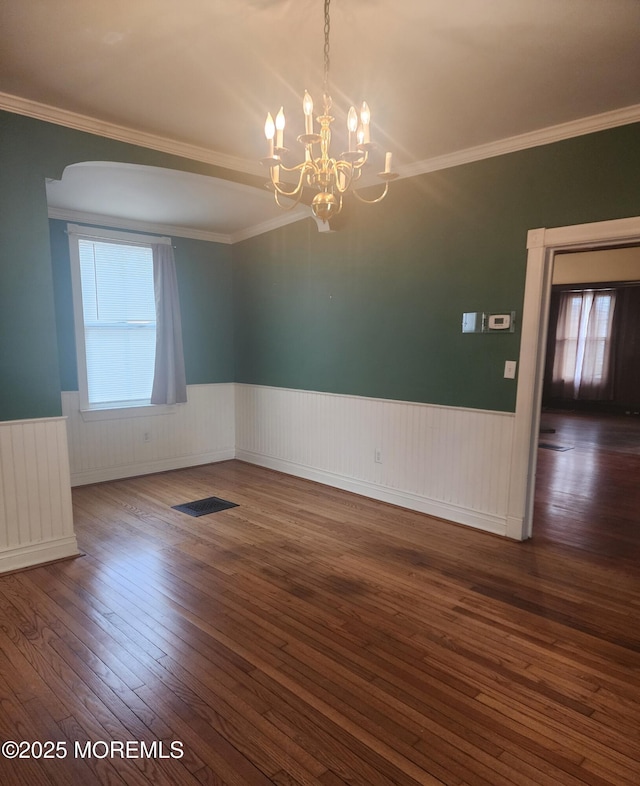 empty room with radiator heating unit, ornamental molding, wainscoting, an inviting chandelier, and hardwood / wood-style flooring