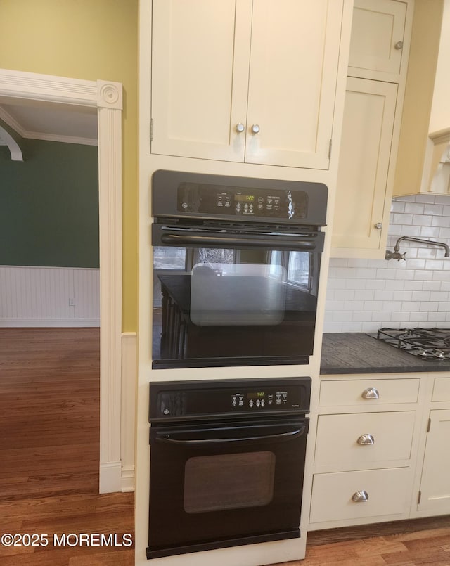 kitchen with dark countertops, wood finished floors, white cabinetry, gas stovetop, and wainscoting