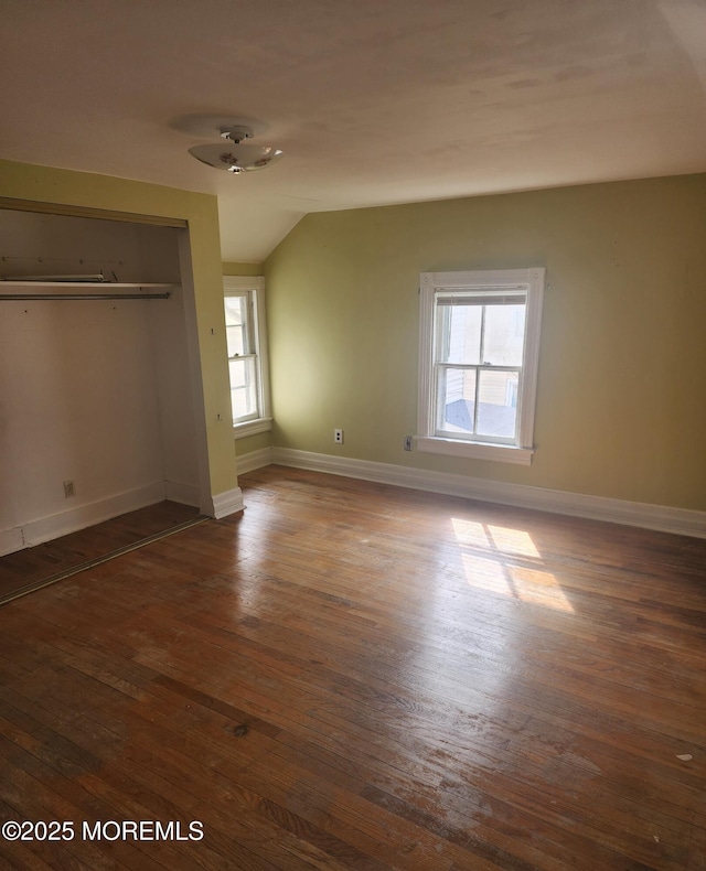 unfurnished bedroom with hardwood / wood-style floors, vaulted ceiling, baseboards, and a closet