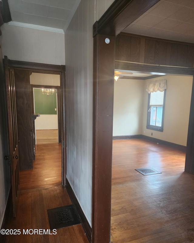 hallway with visible vents, dark wood-type flooring, a chandelier, and crown molding