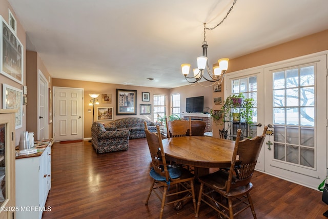 dining space featuring a brick fireplace, dark wood-type flooring, and an inviting chandelier