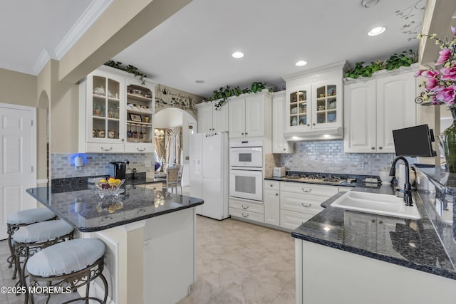 kitchen featuring a kitchen bar, sink, kitchen peninsula, white appliances, and white cabinets