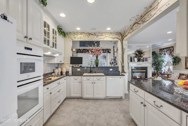 kitchen featuring sink, dark stone countertops, white appliances, a fireplace, and white cabinets