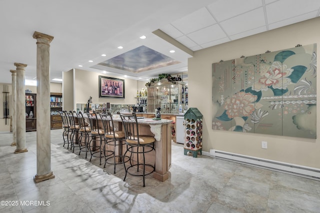 bar featuring a baseboard radiator, a raised ceiling, and ornate columns