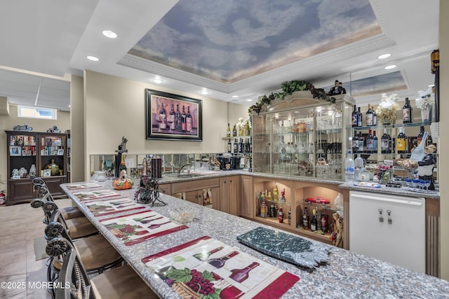 bar featuring light stone counters, sink, crown molding, and a raised ceiling