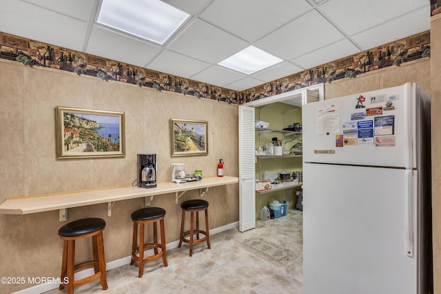 kitchen with white refrigerator, a paneled ceiling, and a kitchen breakfast bar