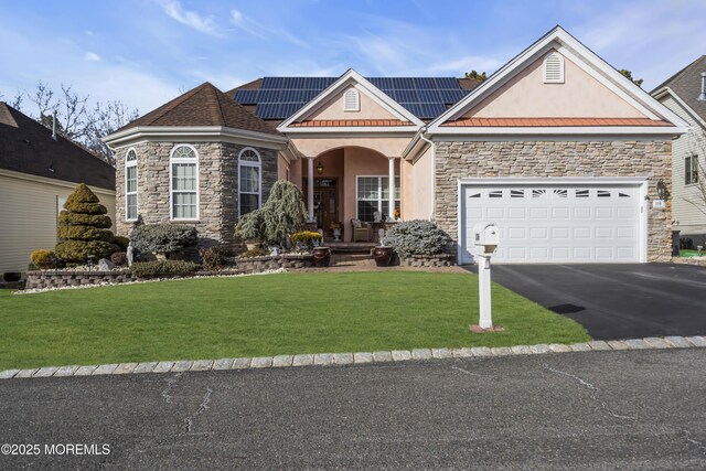 view of front of property with a garage, covered porch, a front lawn, and solar panels