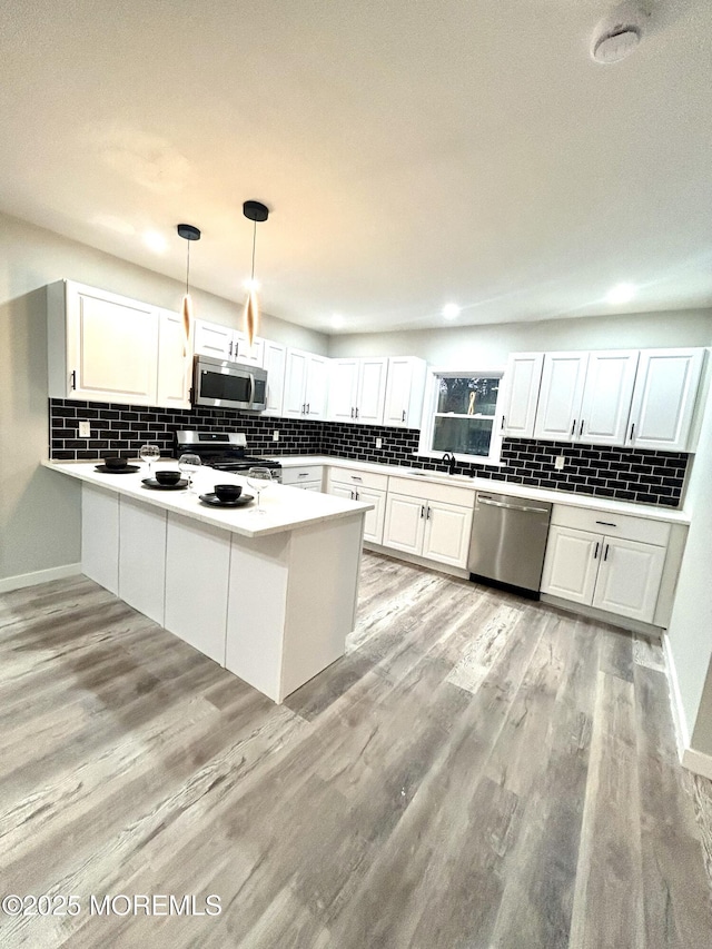 kitchen with white cabinets, hanging light fixtures, kitchen peninsula, stainless steel appliances, and light hardwood / wood-style flooring