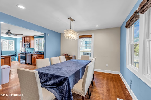 dining space with ceiling fan with notable chandelier and light hardwood / wood-style flooring