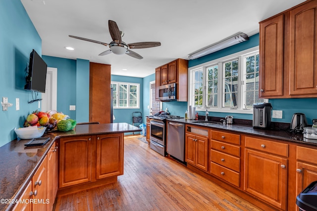 kitchen featuring appliances with stainless steel finishes, sink, dark stone counters, ceiling fan, and light hardwood / wood-style flooring