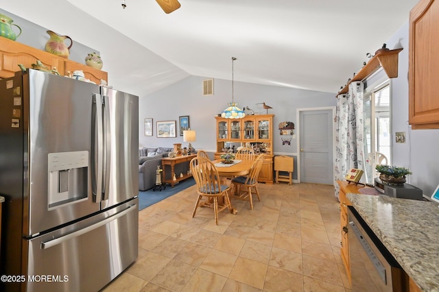 kitchen featuring light stone counters, stainless steel fridge, decorative light fixtures, and vaulted ceiling