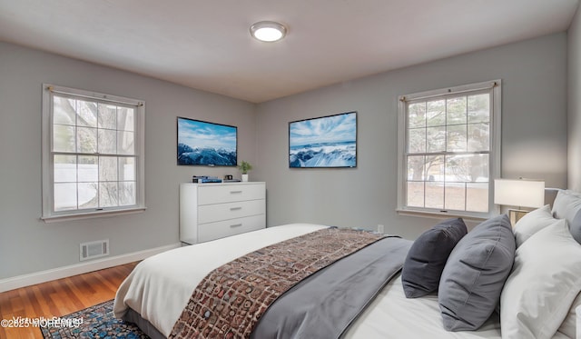 bedroom with visible vents, multiple windows, baseboards, and wood finished floors