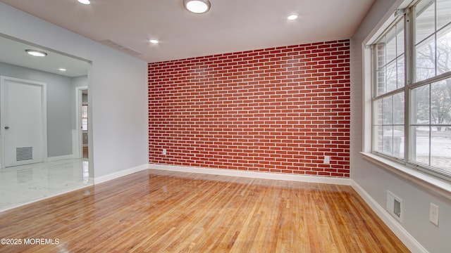 spare room featuring light wood-type flooring and brick wall