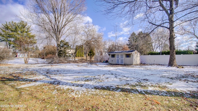 yard layered in snow featuring an outbuilding, a storage shed, and fence