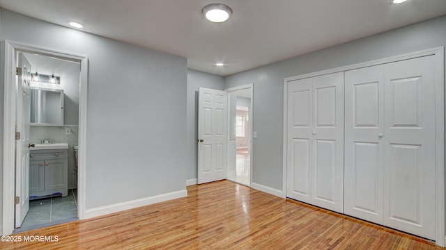 unfurnished bedroom featuring sink, ensuite bathroom, a closet, and light wood-type flooring