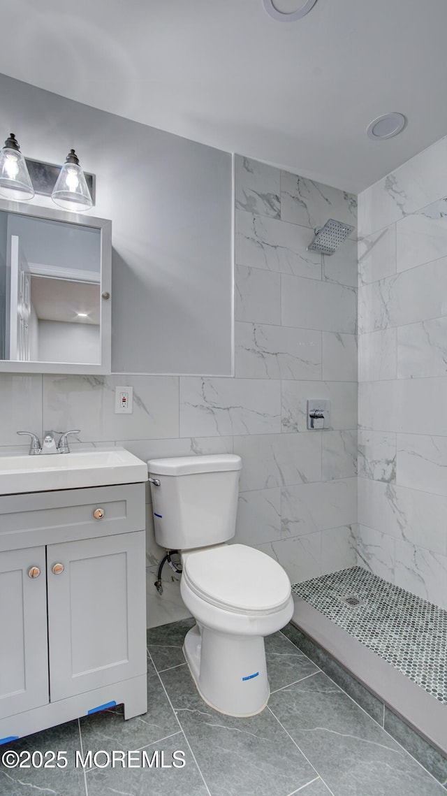 full bath with toilet, marble finish floor, a tile shower, tile walls, and vanity