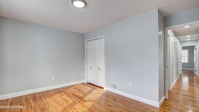 empty room featuring light wood-type flooring, visible vents, baseboards, and attic access