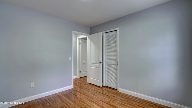 unfurnished bedroom with wood finished floors, baseboards, and a closet