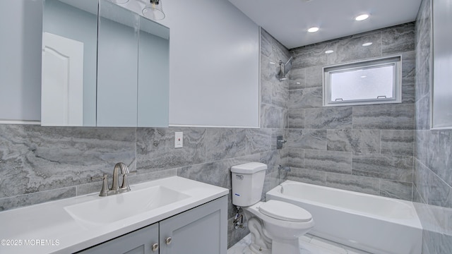 full bathroom with tiled shower / bath, tile walls, vanity, and toilet