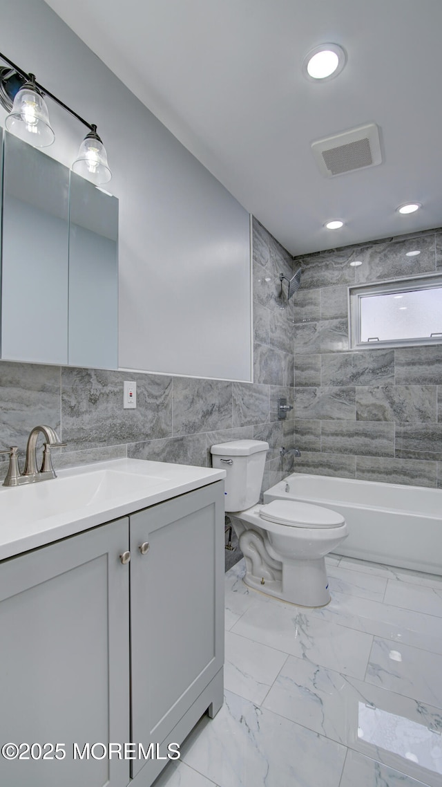 full bathroom with vanity, tiled shower / bath, tile walls, and toilet