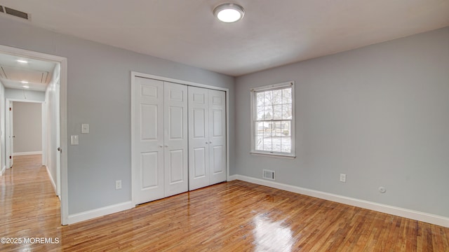 unfurnished bedroom with light wood finished floors, visible vents, attic access, and baseboards