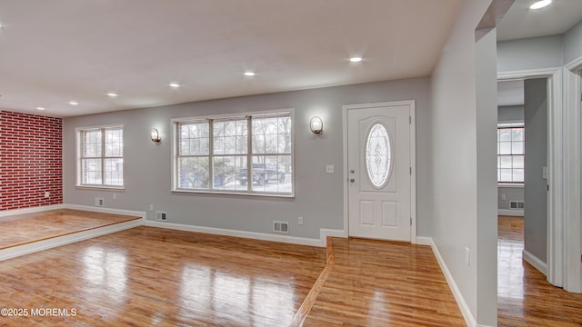 foyer entrance with brick wall and light hardwood / wood-style flooring