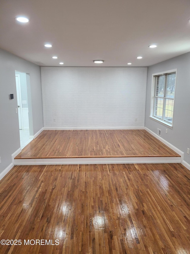 empty room with hardwood / wood-style floors, baseboards, visible vents, brick wall, and recessed lighting