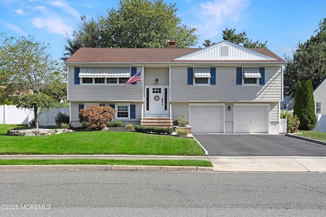 split foyer home featuring a chimney, an attached garage, a front yard, fence, and driveway