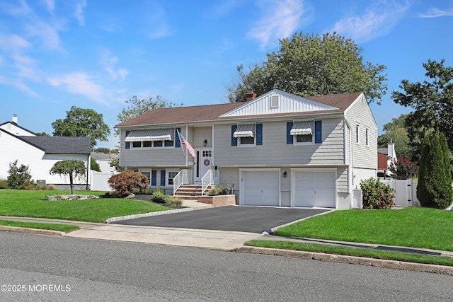 split foyer home featuring an attached garage, a chimney, a front lawn, and aphalt driveway