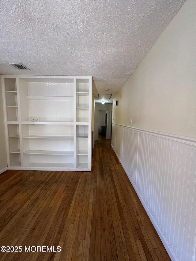 hall featuring dark wood-type flooring, built in features, and a textured ceiling