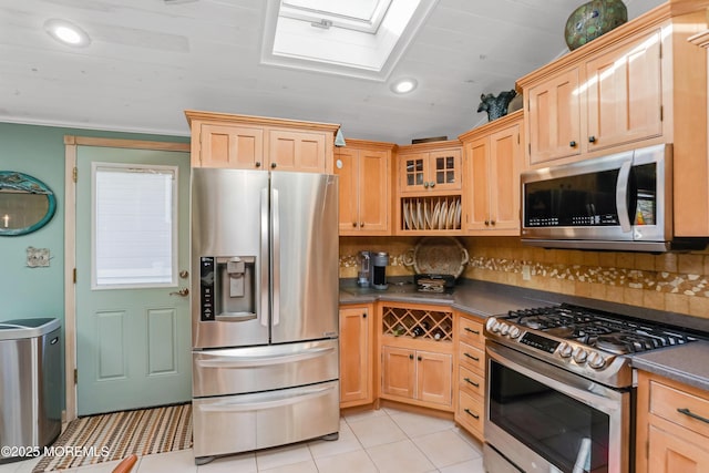 kitchen with light tile patterned floors, appliances with stainless steel finishes, a skylight, tasteful backsplash, and light brown cabinets