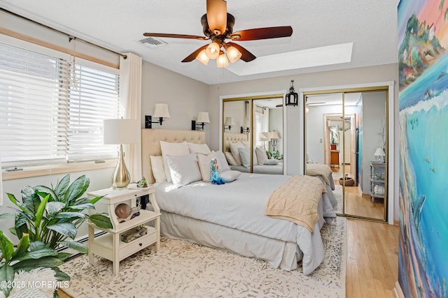 bedroom featuring light hardwood / wood-style flooring, ceiling fan, a skylight, a textured ceiling, and multiple closets