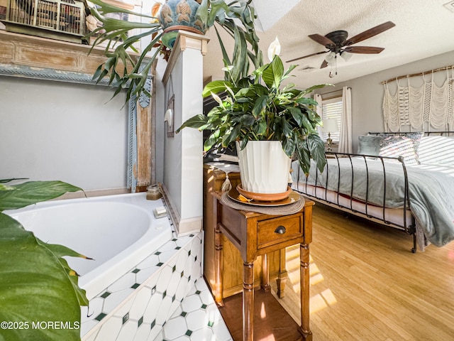 interior space featuring ceiling fan, hardwood / wood-style floors, a textured ceiling, and a tub to relax in