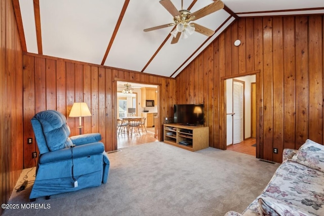 living room with light carpet, high vaulted ceiling, ceiling fan, and wood walls