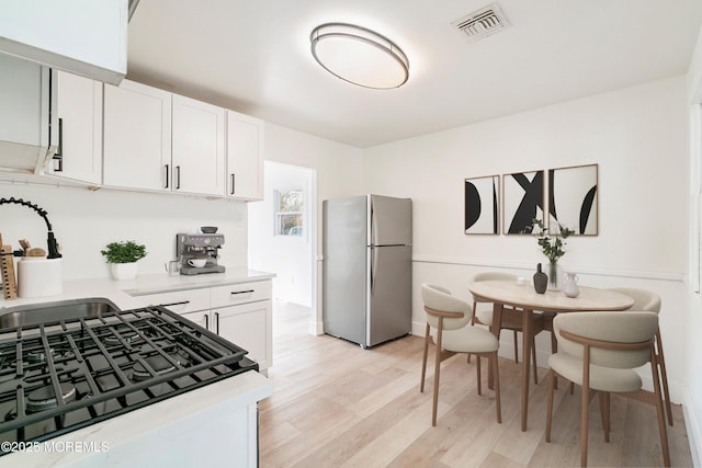 kitchen featuring sink, stainless steel refrigerator, range with gas stovetop, light hardwood / wood-style floors, and white cabinets