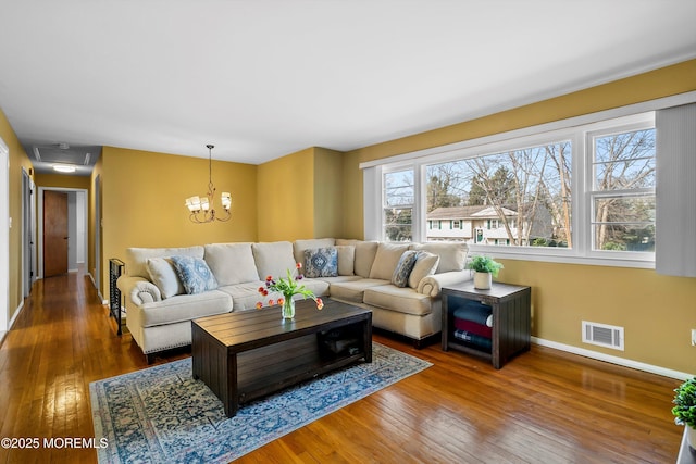 living area featuring an inviting chandelier, wood-type flooring, visible vents, and baseboards