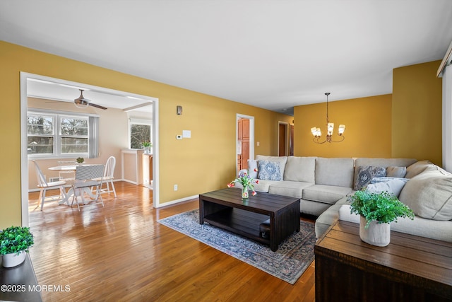 living room featuring ceiling fan with notable chandelier, wood finished floors, and baseboards