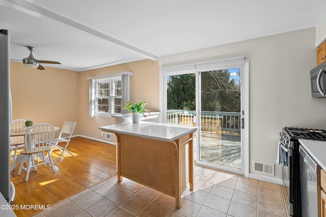 kitchen with light tile patterned floors, visible vents, range with gas stovetop, light countertops, and stainless steel microwave