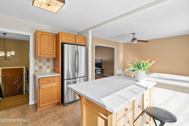 kitchen featuring decorative backsplash, freestanding refrigerator, light tile patterned flooring, light countertops, and ceiling fan with notable chandelier