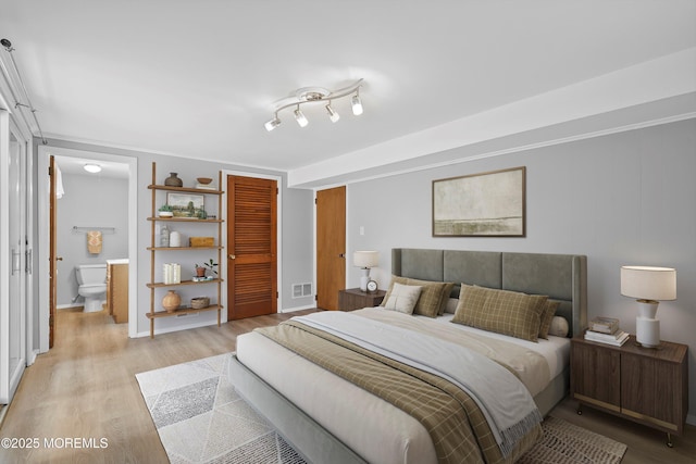 bedroom with a closet, visible vents, light wood-style flooring, and ensuite bath