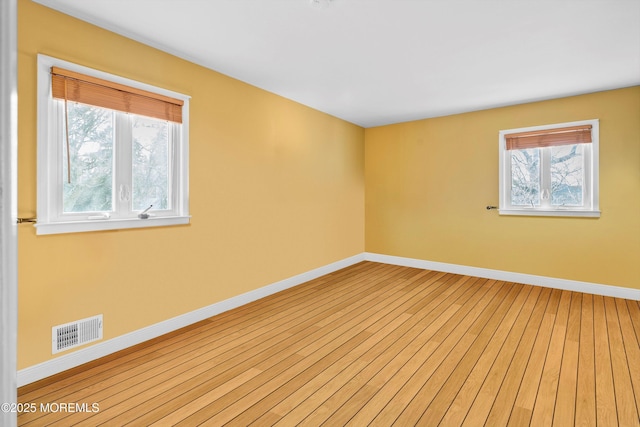 unfurnished room with visible vents, light wood finished floors, and baseboards