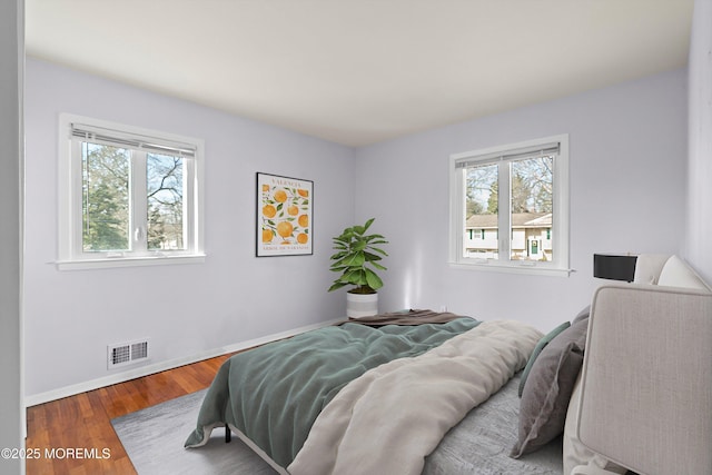 bedroom featuring multiple windows, wood finished floors, visible vents, and baseboards