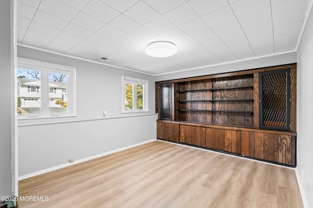 empty room with ornamental molding, wood finished floors, visible vents, and baseboards