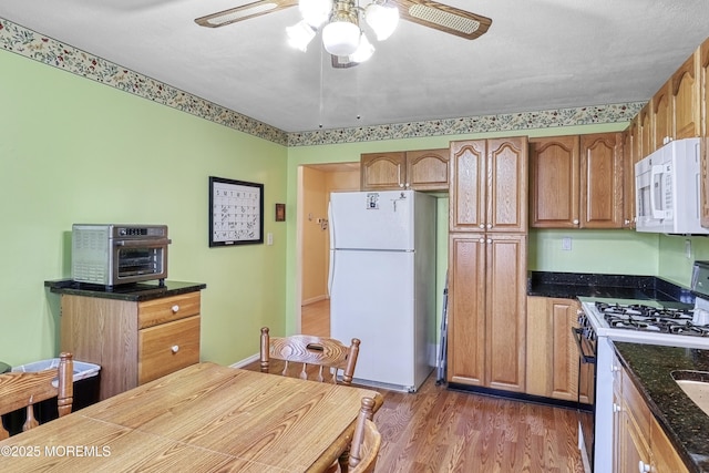 kitchen with ceiling fan, dark hardwood / wood-style floors, dark stone countertops, and white appliances