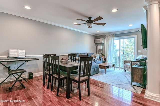 dining room featuring crown molding, a wall mounted air conditioner, wood-type flooring, and ornate columns