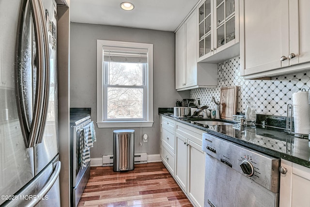 kitchen with appliances with stainless steel finishes, tasteful backsplash, white cabinetry, dark stone counters, and baseboard heating