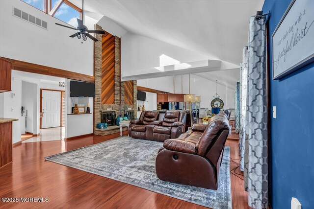 living room featuring high vaulted ceiling, light hardwood / wood-style floors, a large fireplace, and ceiling fan